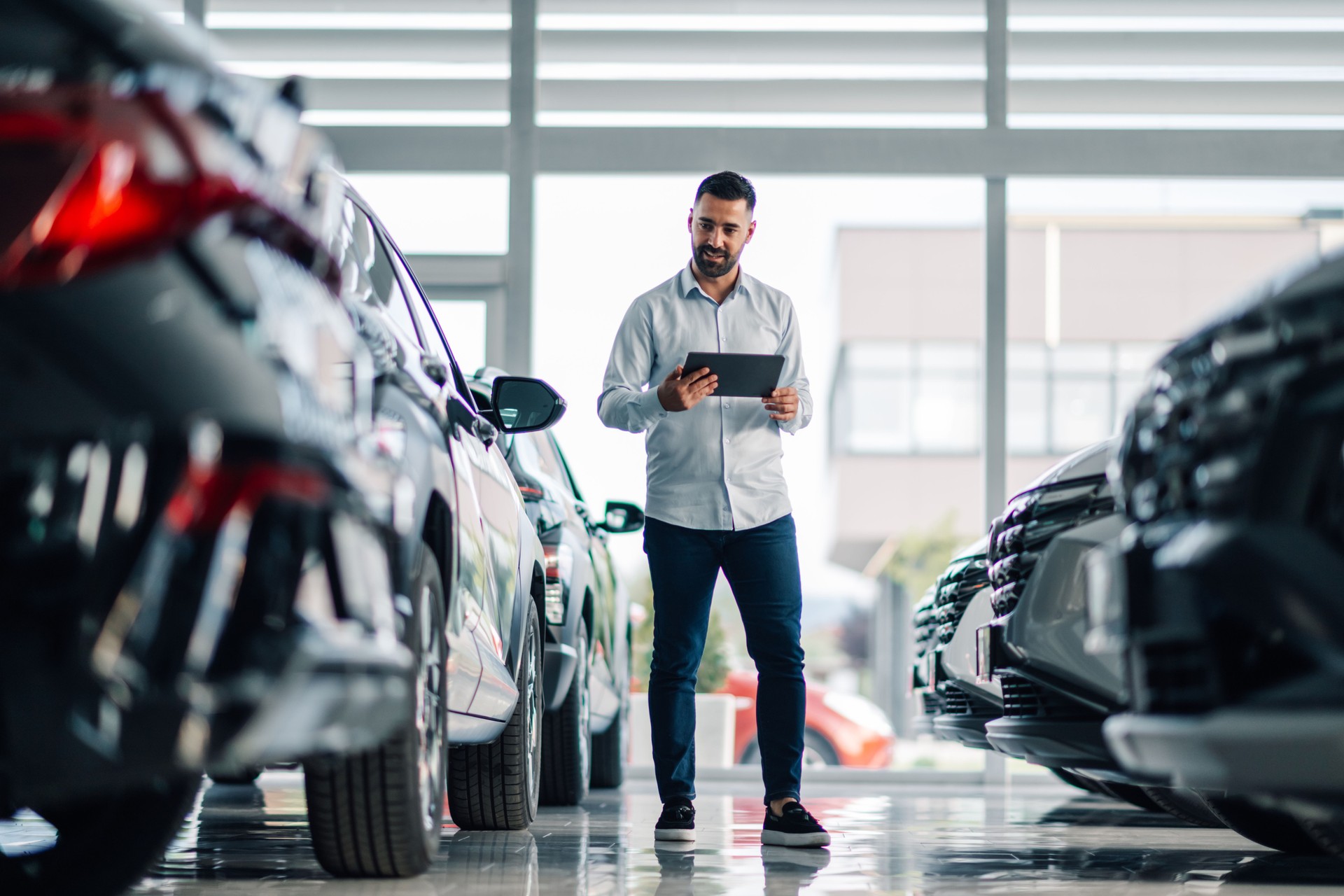 Man using tablet to inspect cars in dealership's showcase area.